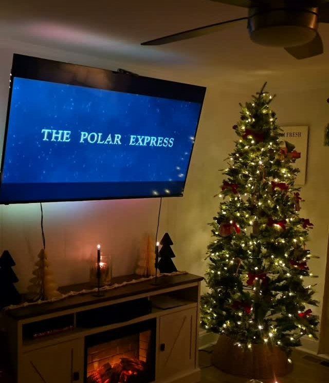 Television showing The Polar Express next to a lit Christmas tree and fireplace.