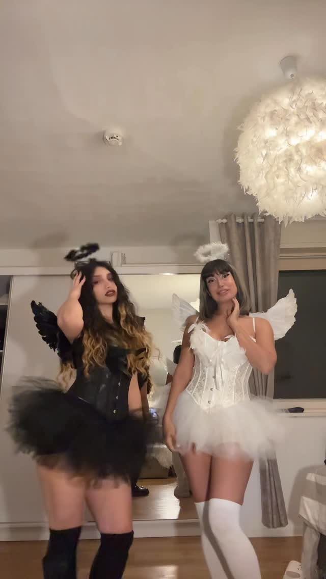 Two women wearing contrasting black and white angel costumes with wings and halos.
