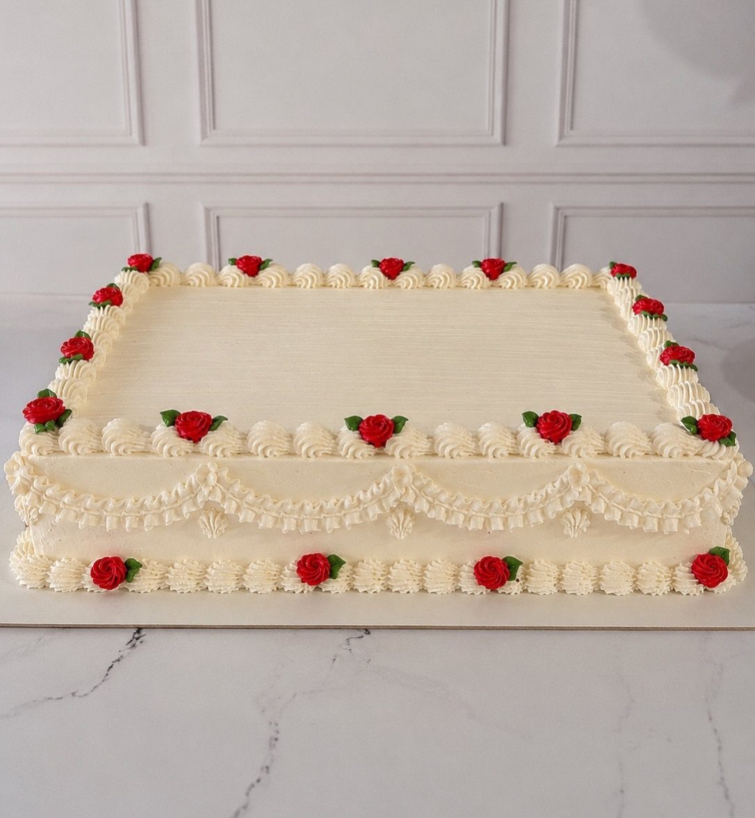 Square white cake with red roses and piped shell borders on a marble surface