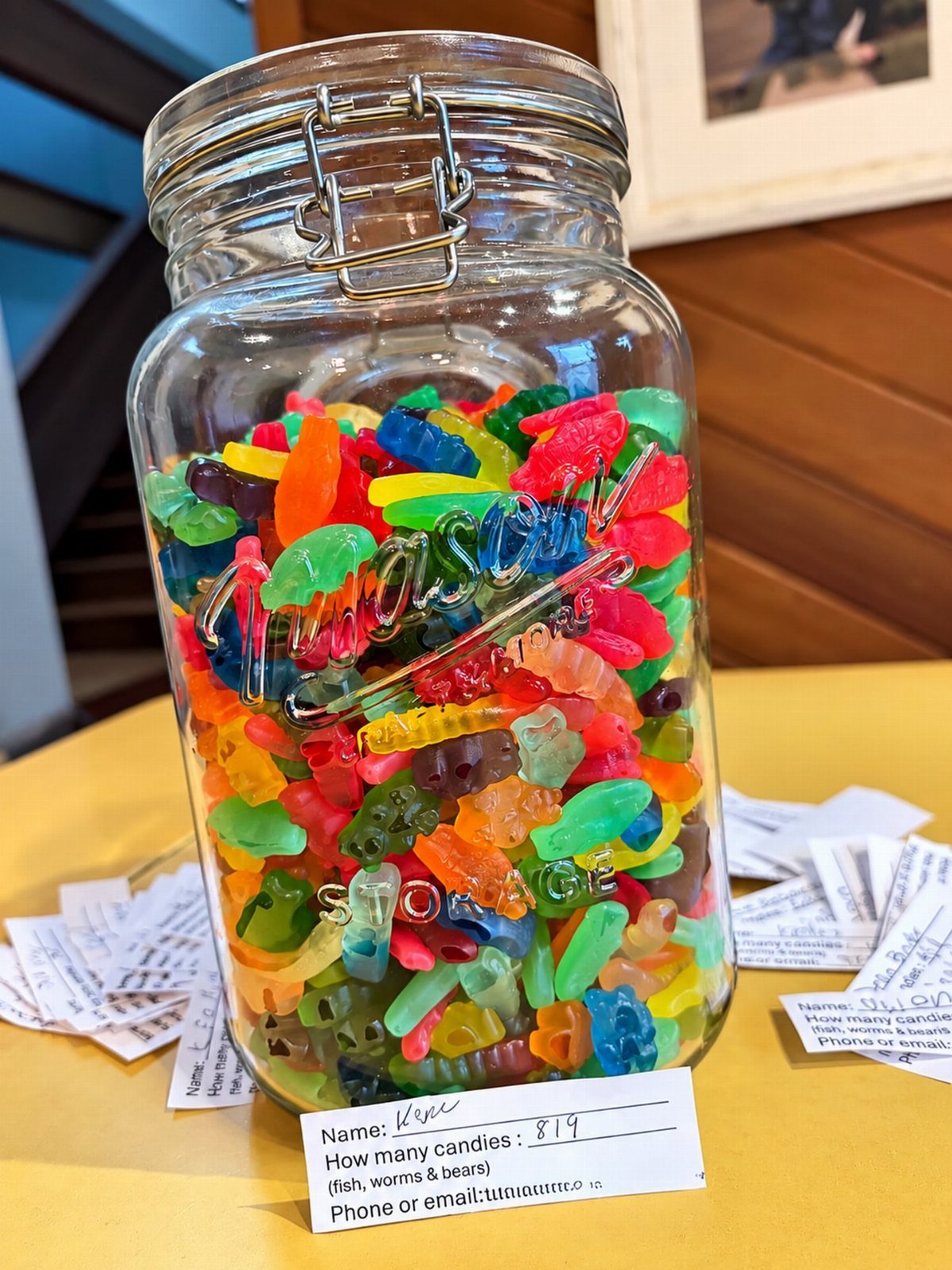 Glass jar filled with colorful gummy candies next to guessing game entry slips.