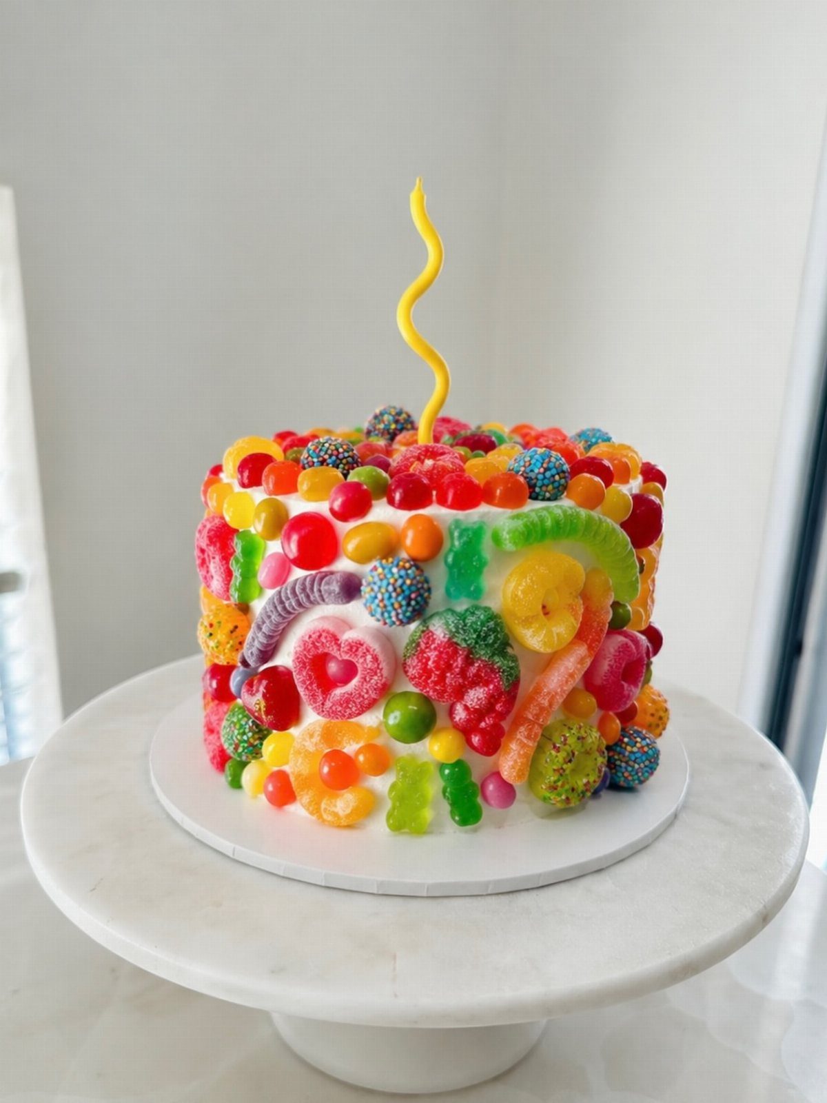 21 Cake Decoration Ideas for Every Skill Level 5 White frosted cake covered in colorful gummy candies with a yellow spiral candle.