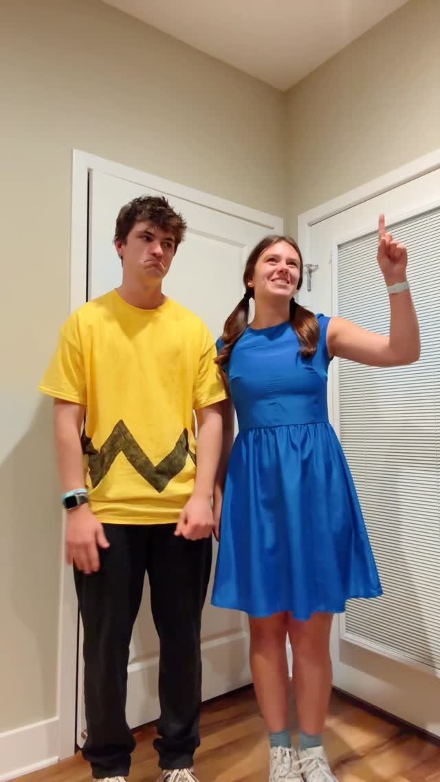 Man in yellow zigzag shirt and woman in blue dress posing as Peanuts characters.