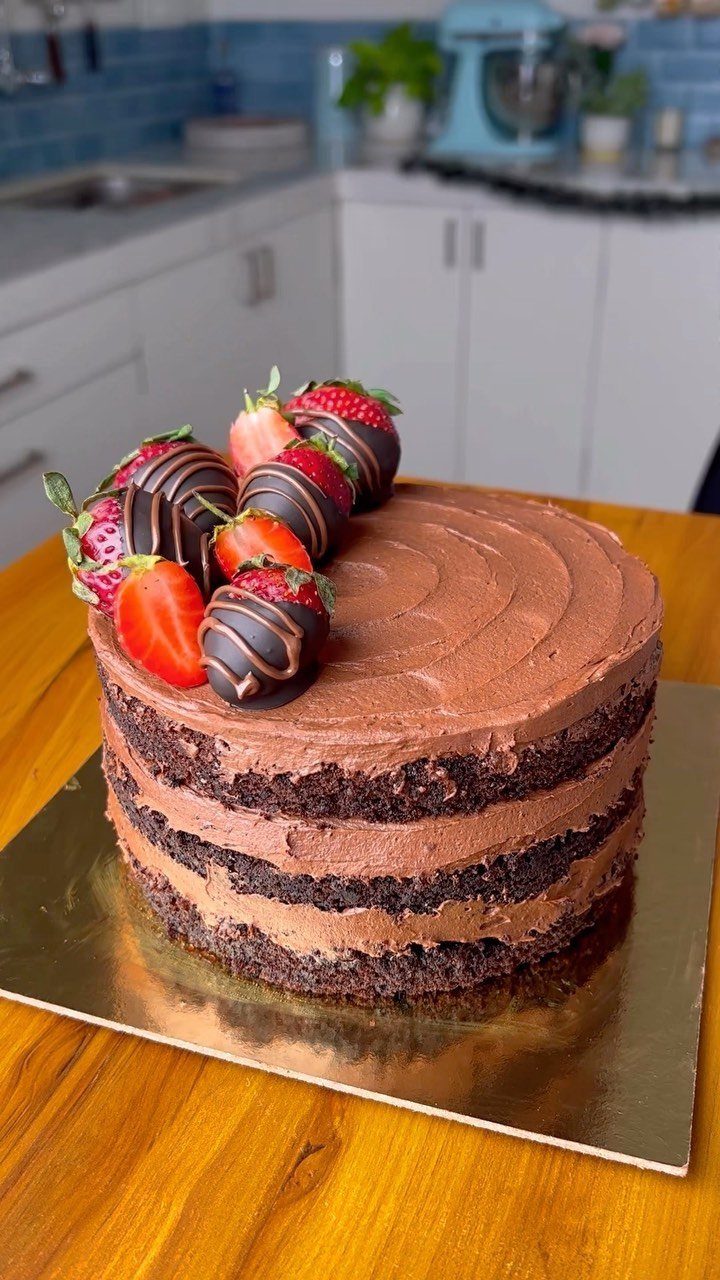 Three-layer chocolate cake topped with chocolate-dipped strawberries on a gold cake board.