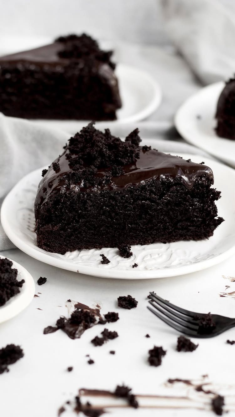 Chocolate cake slice with glossy chocolate ganache topping on a white plate.