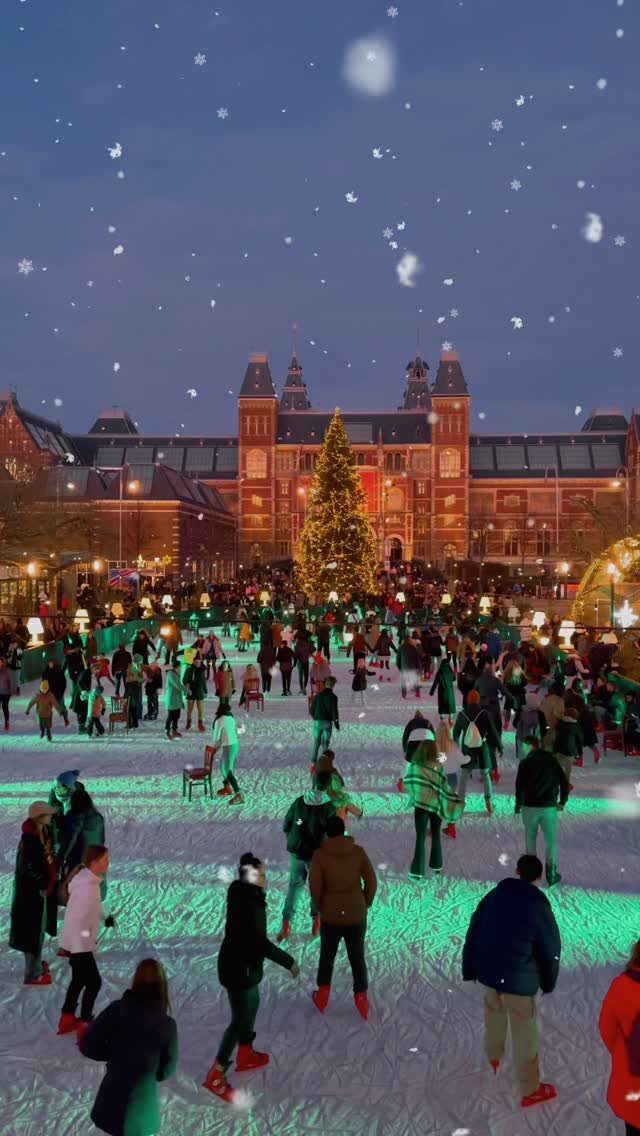 People ice skating on an outdoor rink with a large Christmas tree and building.