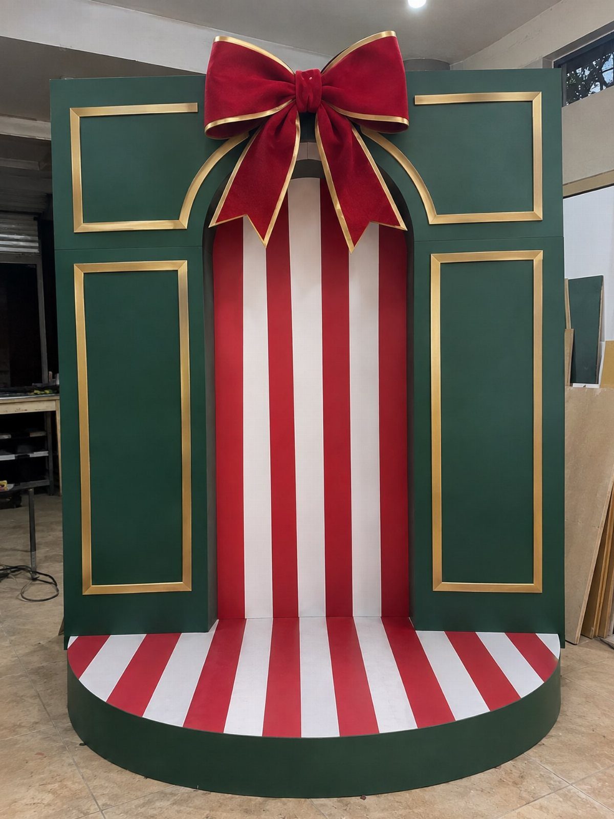 Christmas photo booth backdrop with green panels, red stripes, and a large red bow.