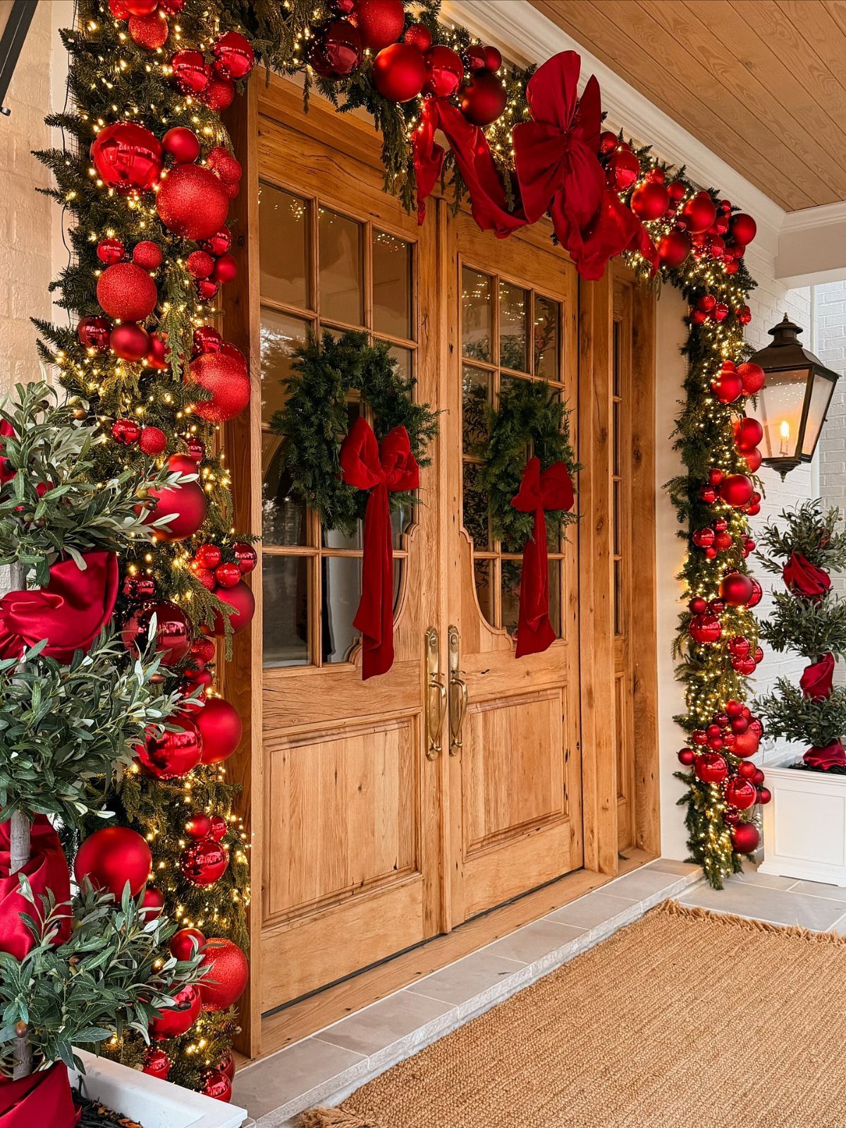36 Christmas Decor Ideas for the Home: Doors, Tables, Trees & More 2 Wooden double doors framed by a festive garland with red ornaments and wreaths.