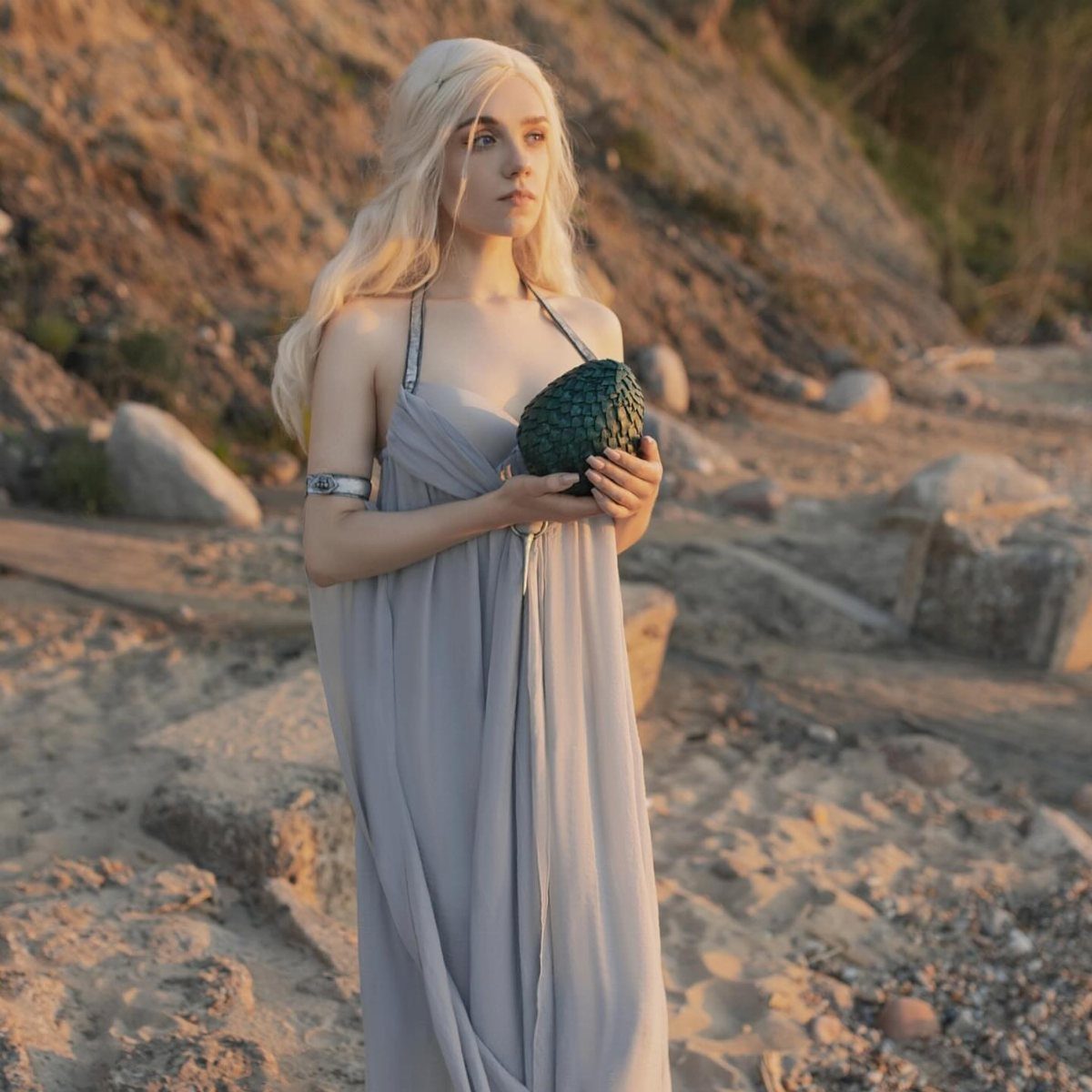 Woman in a purple gown holding a dragon egg on a sandy beach