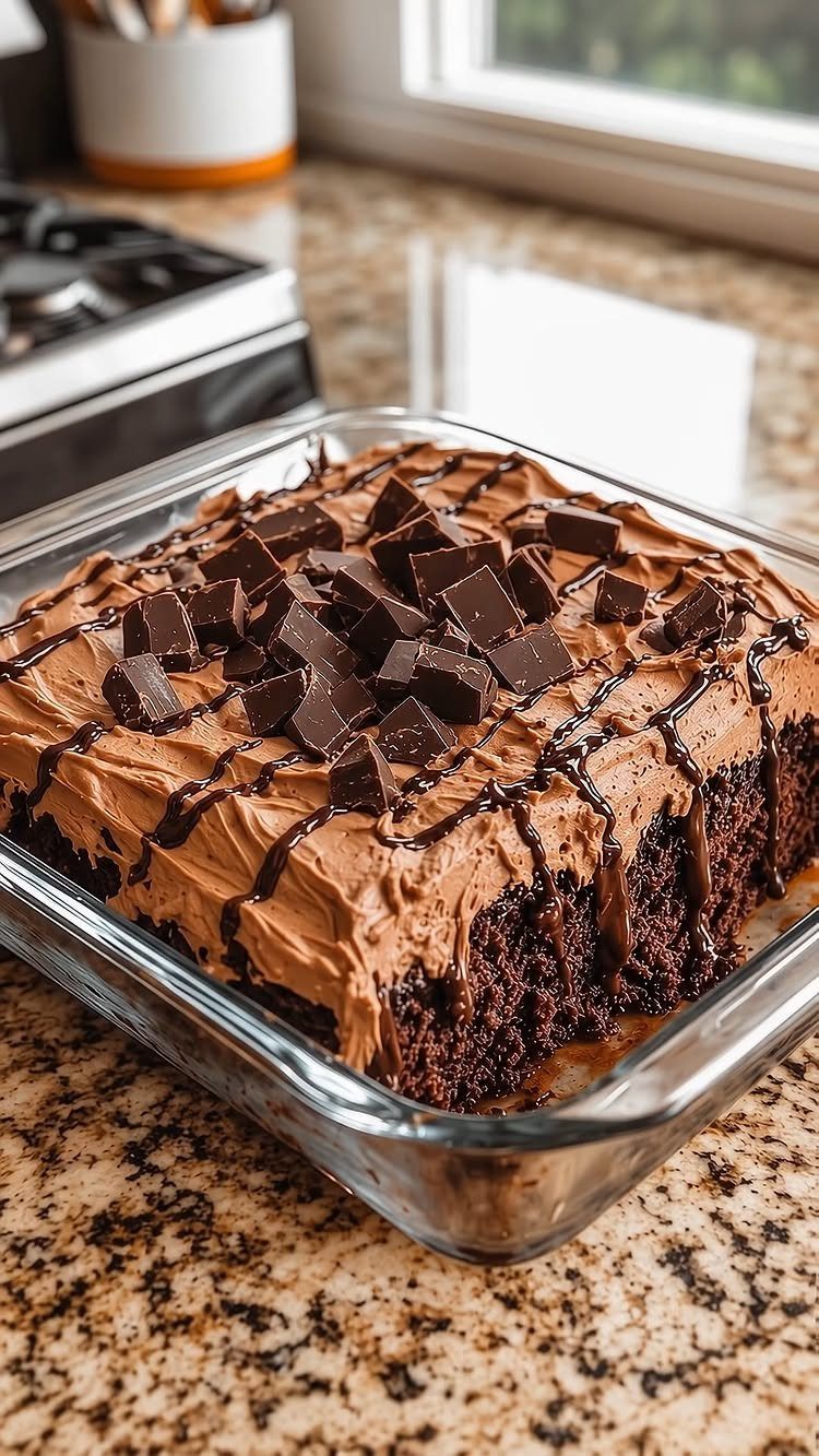 Dark chocolate cake with chocolate frosting and chunks in a glass dish.