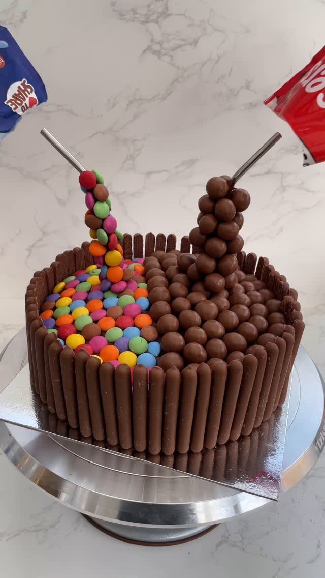 Round cake decorated with chocolate fingers, colorful candies, and brown chocolate spheres.