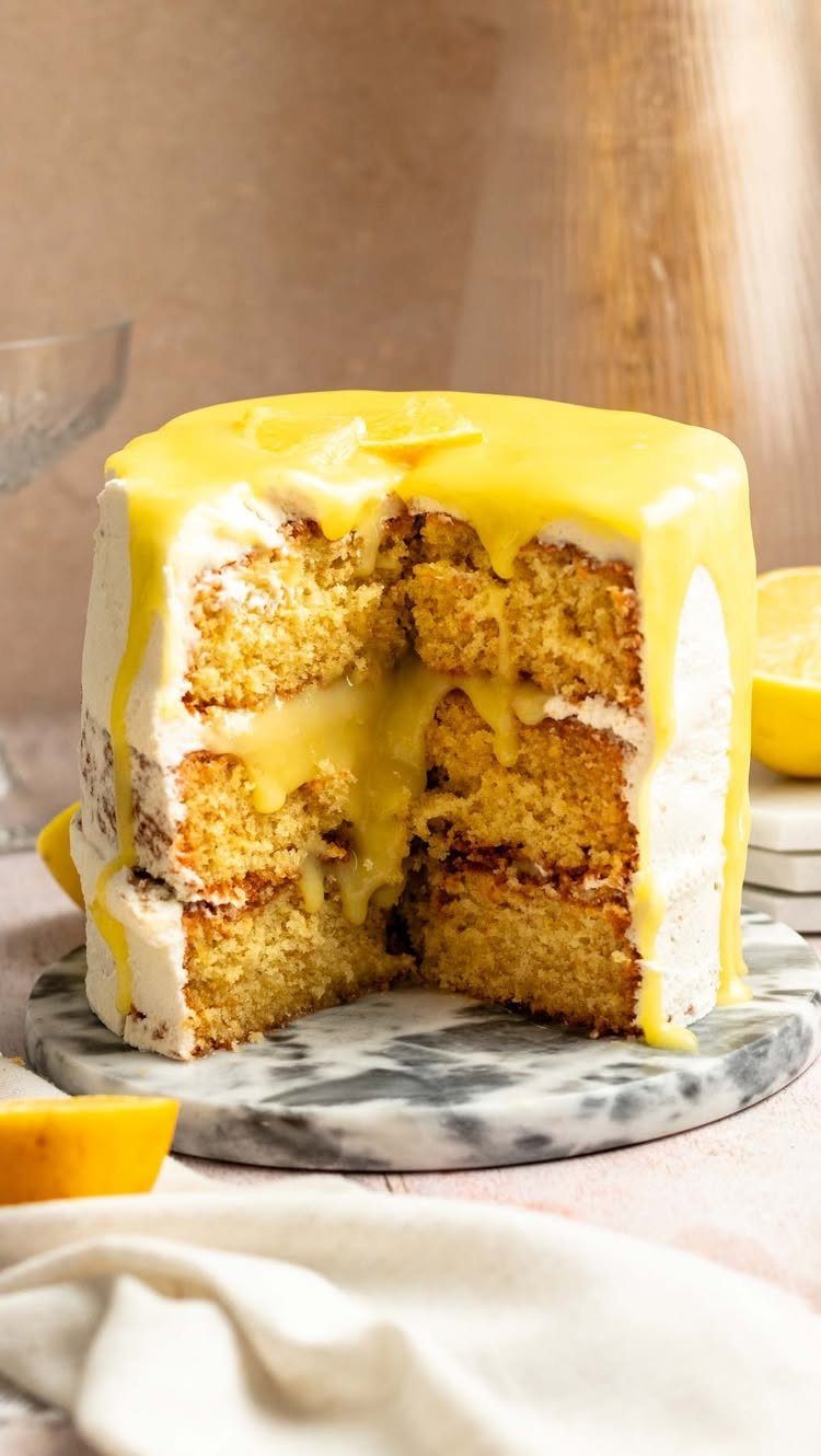 Three-layer sponge cake with white frosting and dripping yellow lemon curd glaze.