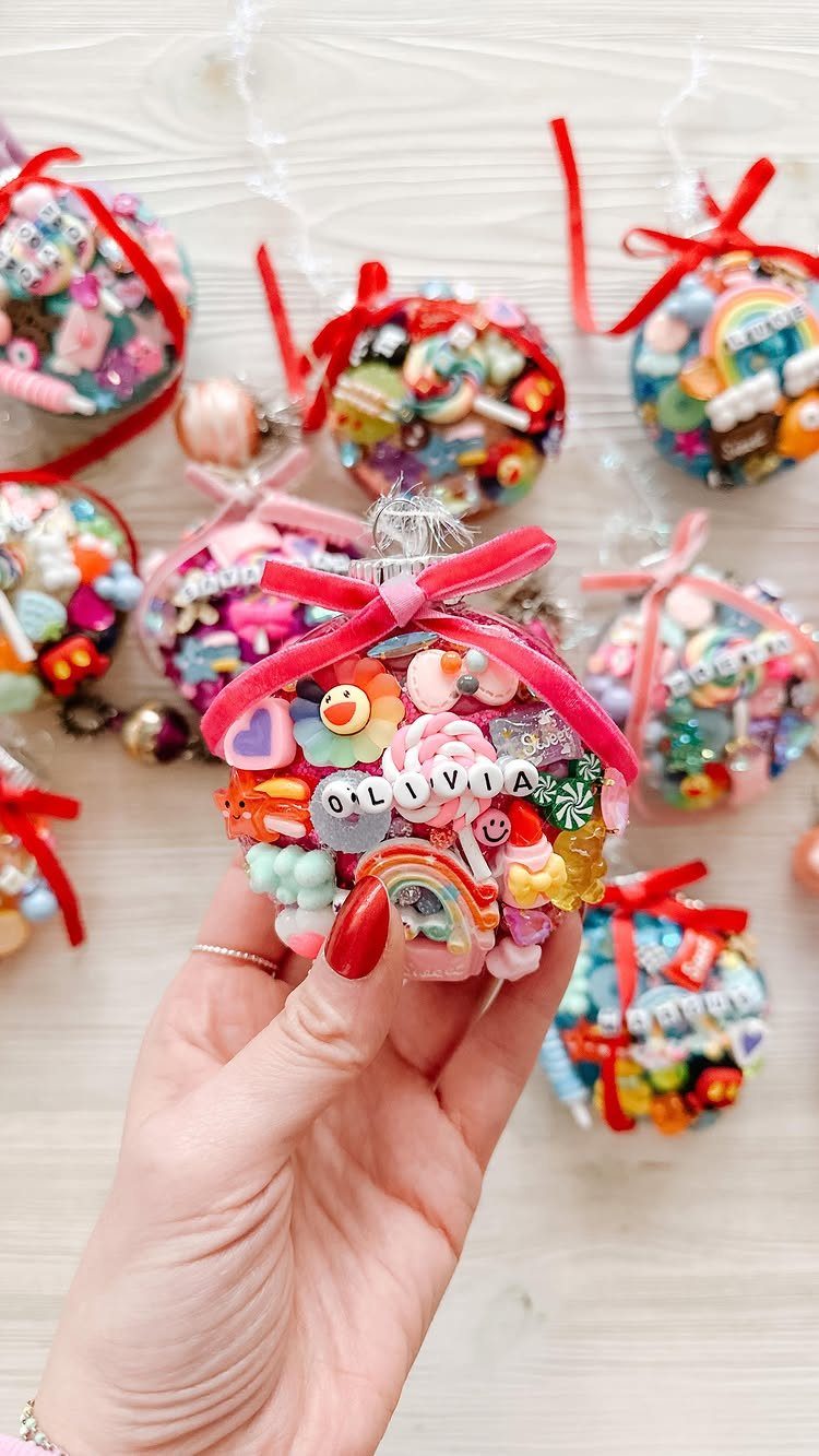 Hand holding a colorful personalized Christmas ornament with charms on a wooden background