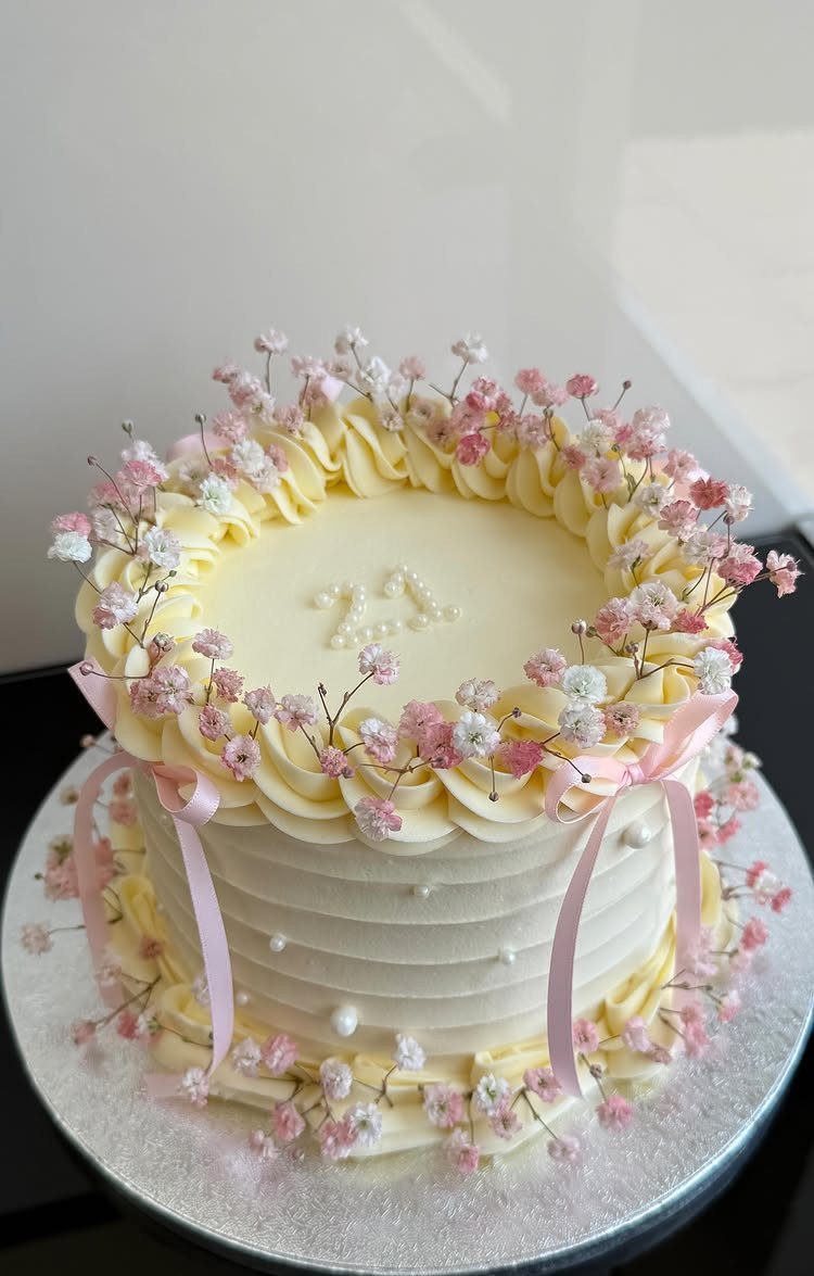 White frosted birthday cake decorated with pink flowers, pearls, and pink ribbons.