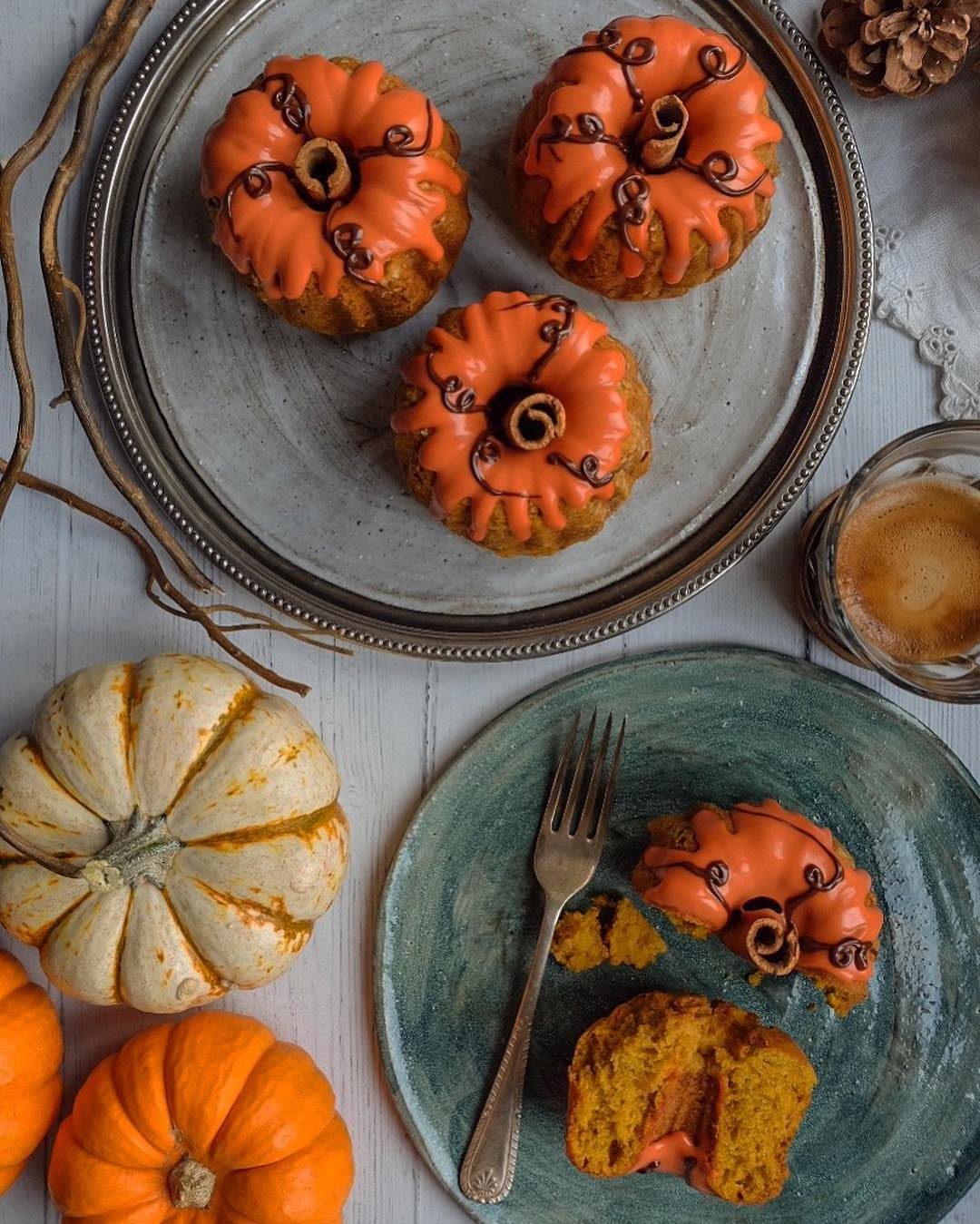 Pumpkin-shaped mini cakes with orange frosting and chocolate swirls on plates.