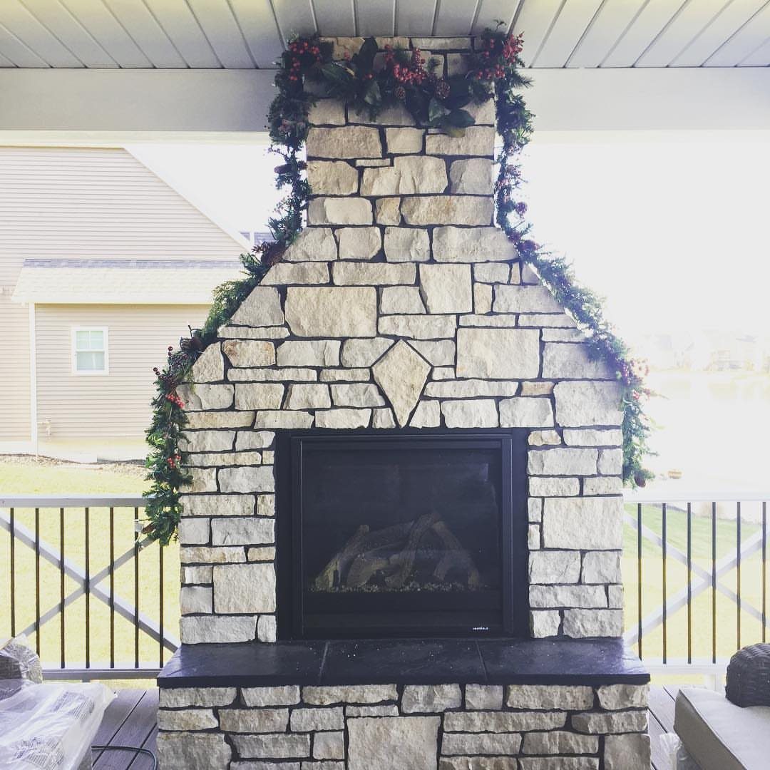 36 Christmas Decor Ideas for the Home: Doors, Tables, Trees & More 19 Outdoor stone fireplace decorated with a green pine garland and red berries.