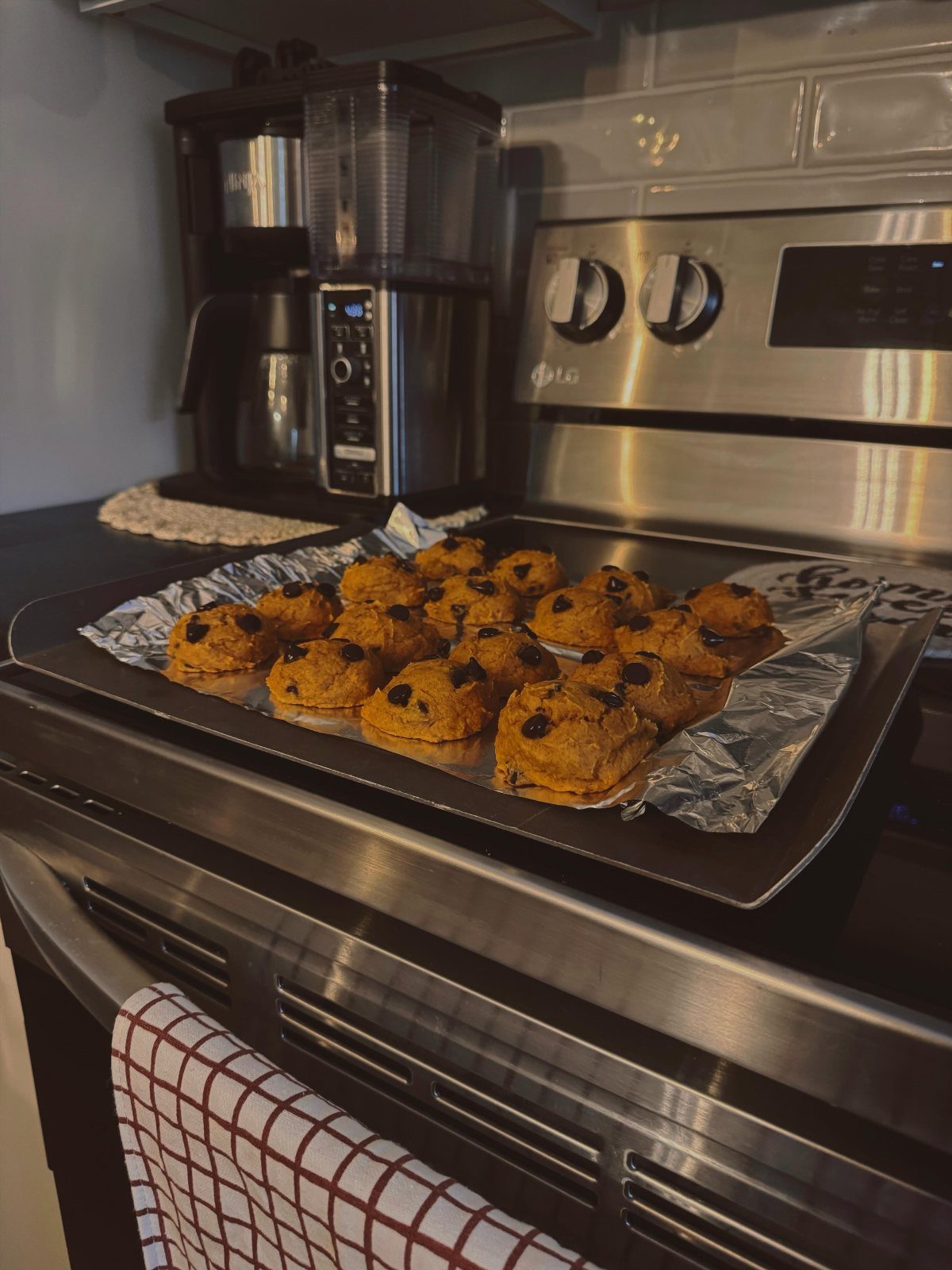 21 Pumpkin Theme Food Ideas for Fall Gatherings 10 Pumpkin chocolate chip cookies on a baking sheet resting on a kitchen oven.