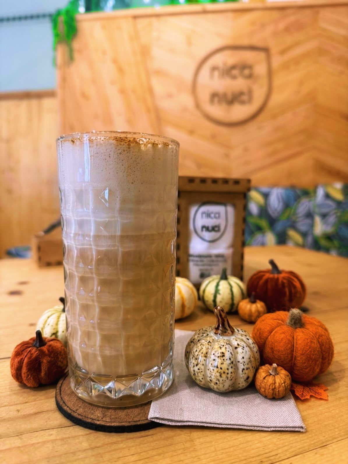 Pumpkin spice latte in a tall glass surrounded by small decorative pumpkins.