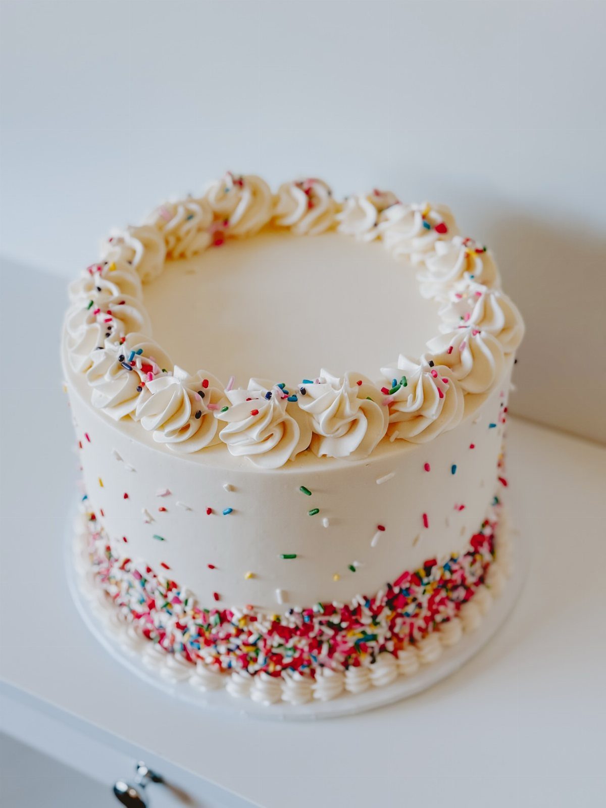 21 Cake Decoration Ideas for Every Skill Level 2 White frosted cake decorated with colorful rainbow sprinkles and piped buttercream swirls.