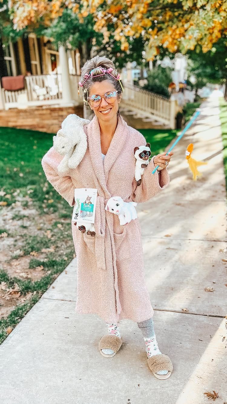 Woman in a pink fluffy bathrobe and slippers holding stuffed animals and a wand.