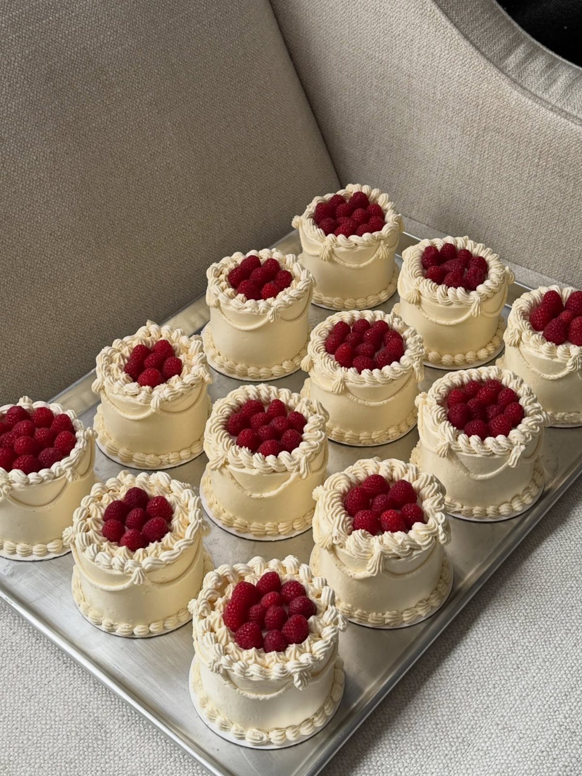 Small white frosted layer cakes topped with fresh raspberries on a silver tray.